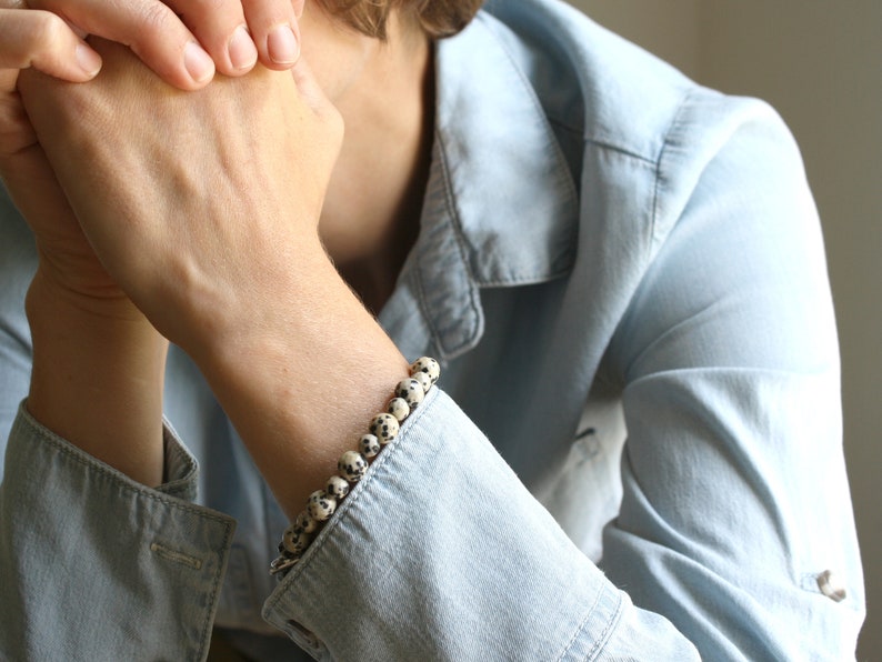 May include: A person wearing a light blue denim shirt with a bracelet made of white and black speckled beads.