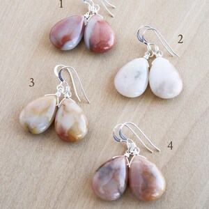 May include: Four pairs of gemstone drop earrings with silver-colored hooks. The earrings feature teardrop-shaped stones in various colors, including white, pink, brown, and yellow. Each pair is unique in color and pattern.