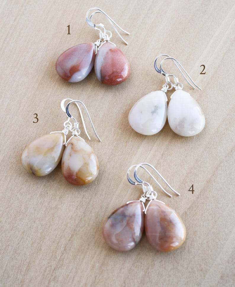 May include: Four pairs of gemstone drop earrings with silver-colored hooks. The earrings feature teardrop-shaped stones in various colors, including white, pink, brown, and yellow. Each pair is unique in color and pattern.