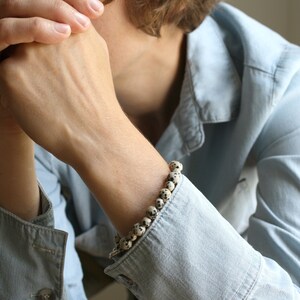 May include: A close-up of a person's wrist wearing a bracelet made of white and black speckled beads.