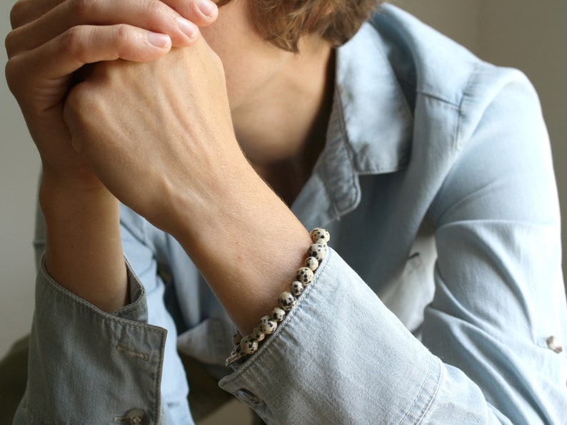 May include: A close-up of a person's wrist wearing a bracelet made of white and black speckled beads.