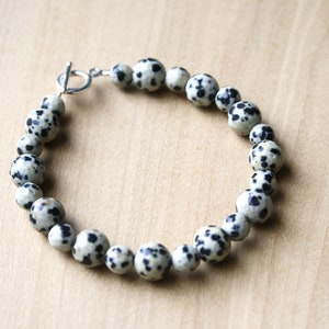 May include: A bracelet made of black and white dalmatian jasper beads with a silver toggle clasp.
