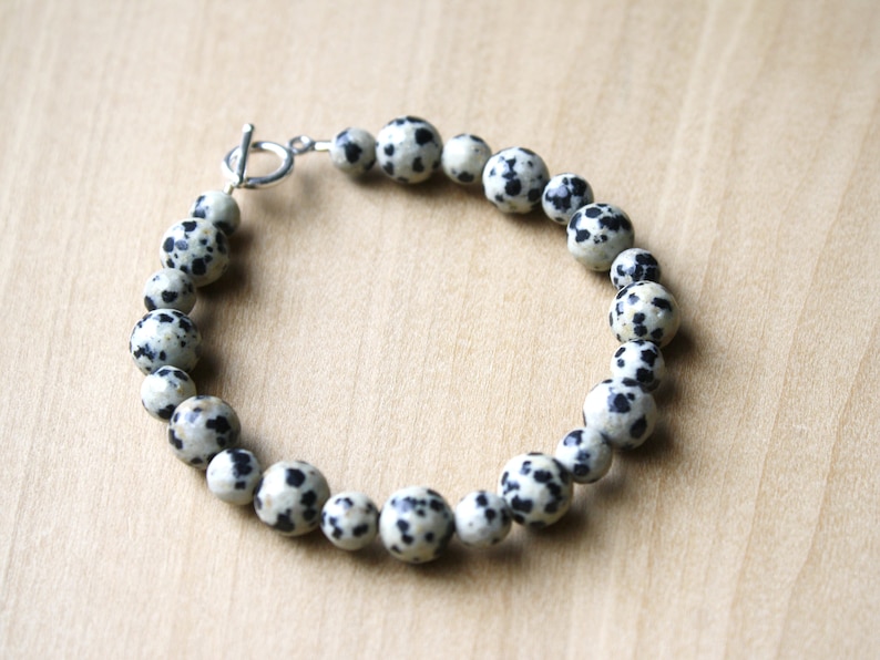 May include: A bracelet made of black and white dalmatian jasper beads with a silver toggle clasp.