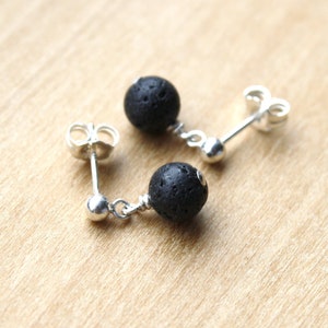 May include: A pair of silver stud earrings with black lava rock beads. The earrings have a simple design and are perfect for everyday wear.