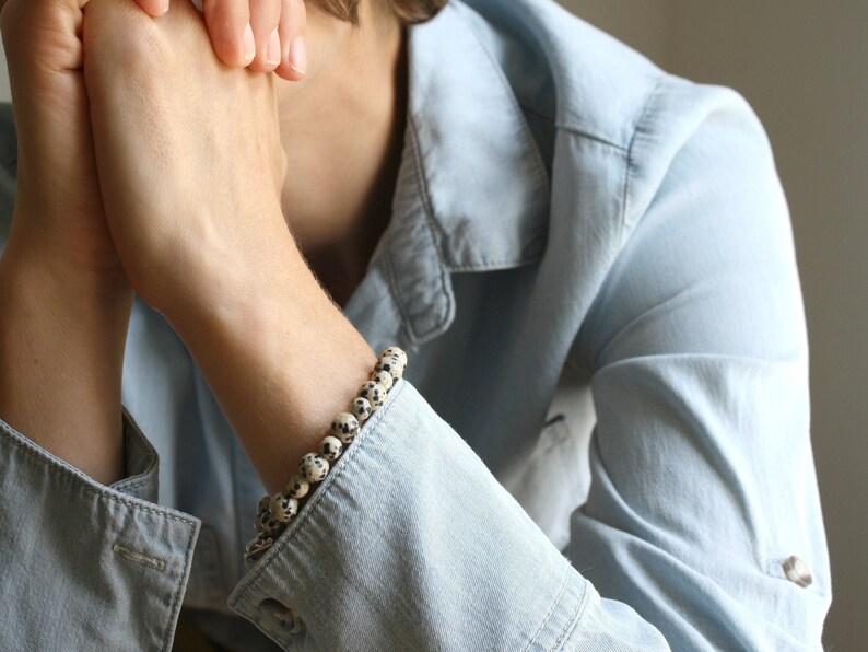 May include: A close-up of a person's wrist wearing a bracelet made of white and black speckled beads.