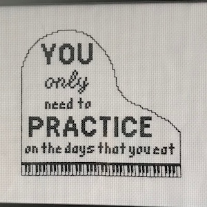 May include: Black and white cross-stitch design in a black frame. The design features a piano with the text "YOU only need to PRACTICE on the days that you eat."