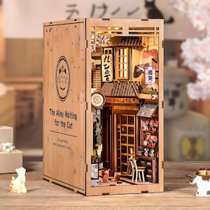 May include: A wooden book nook featuring a miniature Japanese alley scene with illuminated buildings, signs, and small cat figurines. The text "The Alley Waiting for the Cat" is visible on the side.