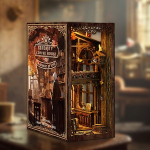 May include: A detailed wooden book nook depicting a coffee house scene with the text "Serenity Coffee House" and "Enjoyment of Life". The interior scene includes a bar, bookshelves, and a figure. The design incorporates warm lighting and intricate details.