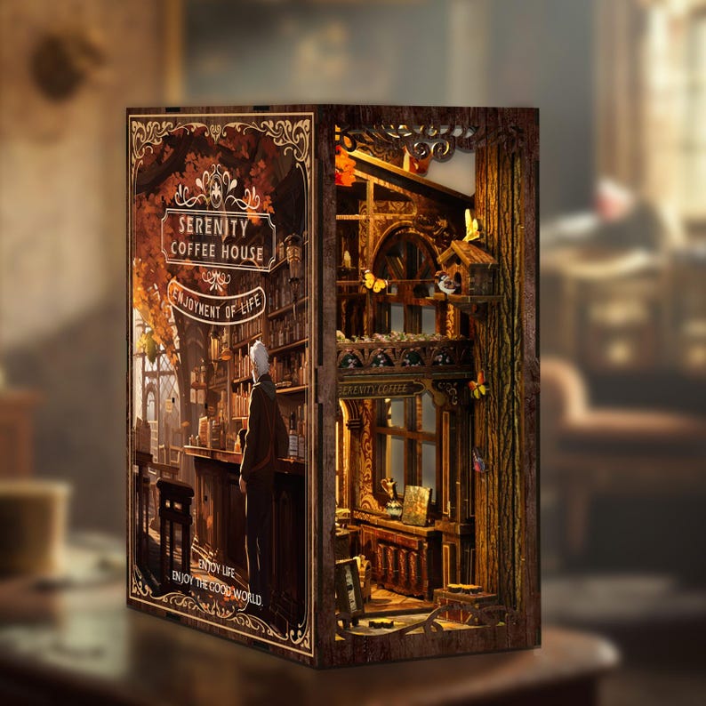 May include: A detailed wooden book nook depicting a coffee house scene with the text "Serenity Coffee House" and "Enjoyment of Life". The interior scene includes a bar, bookshelves, and a figure. The design incorporates warm lighting and intricate details.