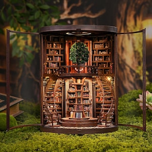 May include: A miniature wooden library with spiral staircases, bookshelves, and a central tree. The interior is illuminated, and the structure is encased in glass doors, set against a backdrop of greenery and moss.