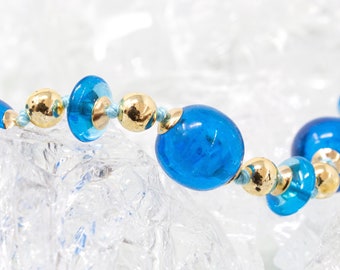 May include: A blue and gold beaded necklace with a variety of sized beads. The beads are made of glass and metal.