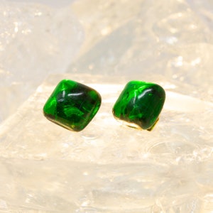 May include: A pair of square-shaped green glass earrings with a swirling pattern. The earrings are set against a white background.