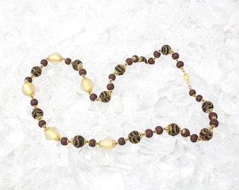 Könnte beinhalten: Eine braune und goldene Perlenkette mit einem gemusterten Design. Die Kette besteht aus runden Perlen und ist auf einer goldenen Kette aufgefädelt.