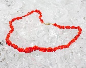 May include: A red coral necklace with a gold clasp, displayed on a bed of crushed ice.