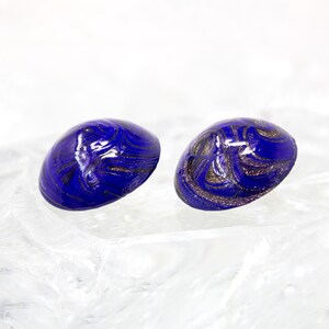 Op de afbeelding: Een paar blauwe glazen oorbellen met gouden swirls. De oorbellen zijn rond en hebben een glanzende afwerking.