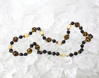 Könnte beinhalten: Eine schwarze und goldene Perlenkette mit abwechselnden schwarzen Perlen und gelben und schwarzen gemusterten Perlen.
