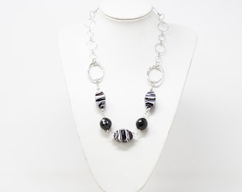 May include: A silver chain necklace with black and white striped oval beads and black round beads.