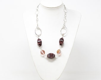 May include: A silver chain necklace with alternating oval-shaped glass beads in shades of pink and clear. The beads have a striped pattern.
