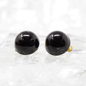 May include: A pair of black clip-on earrings with a round, smooth, and shiny surface.