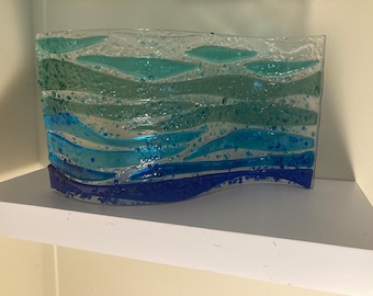 Könnte beinhalten: Eine wellenförmige Glasskulptur mit Schichten aus blauem, grünem und weißem Glas. Das Glas hat eine strukturierte Oberfläche und scheint handgefertigt zu sein.