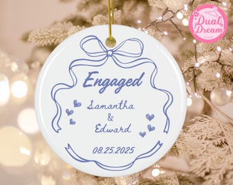 May include: White ceramic ornament with a blue ribbon design and the word "Engaged". The ornament includes the names "Samantha & Edward" and the date "08.25.2025". A gold string is attached for hanging.