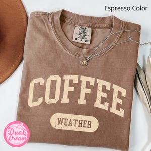 K&ouml;nnte beinhalten: Ein braunes T-Shirt mit dem Text "COFFEE WEATHER" in einer Vintage-Schriftart. Das Shirt ist aus einem weichen, bequemen Material und hat einen Used-Look.