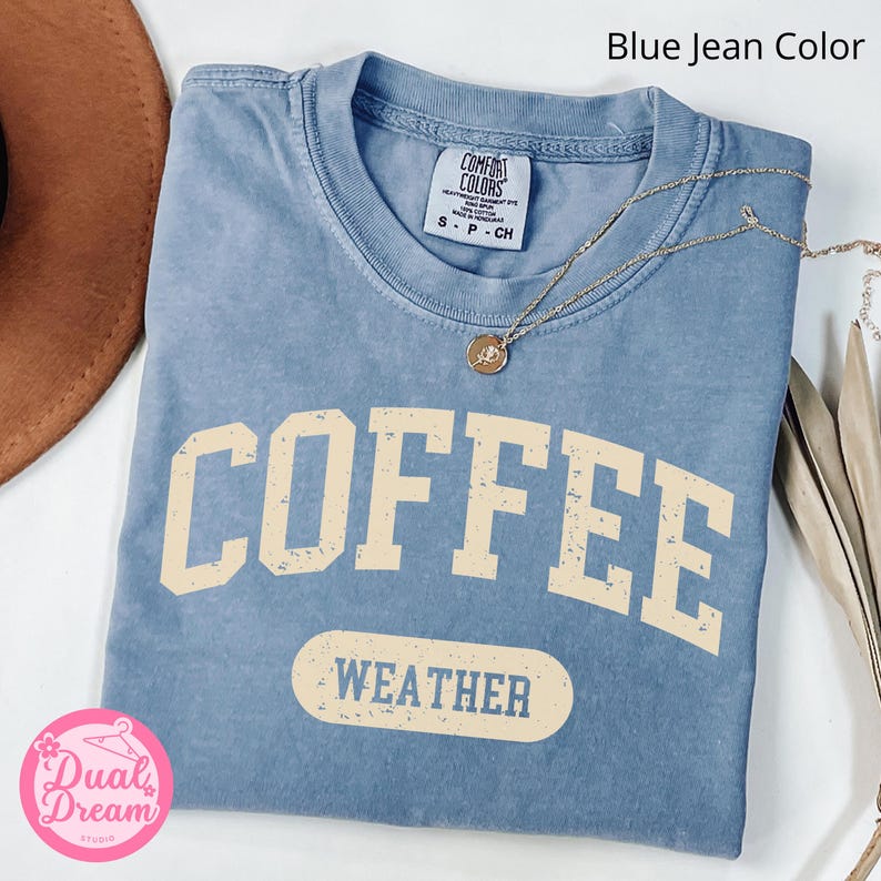K&ouml;nnte beinhalten: Ein T-Shirt in Jeansblau mit dem Text "COFFEE WEATHER" in einer Vintage-Schriftart. Das Shirt ist aus einem weichen, bequemen Material.