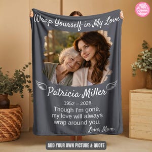 May include: A dark gray rectangular fleece blanket featuring a central photo of two individuals, the text "Wrap Yourself in My Love," the name "Patricia Miller," the dates "1952 – 2026," and the quote "Though I'm gone, my love will always wrap around you. Love, Mom."