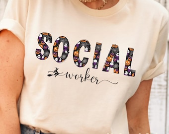 May include: A cream-colored t-shirt featuring the text SOCIAL in large block letters filled with a pattern of orange pumpkins, purple ghosts, and spiderwebs. Below, the word worker is written in black cursive script with a small witch silhouette.