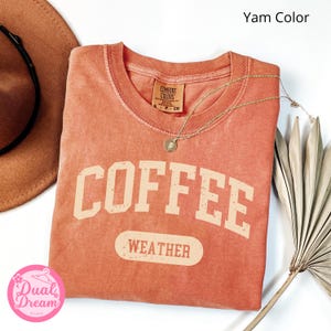 K&ouml;nnte beinhalten: Ein verbrannt-orangenes T-Shirt mit dem Text "COFFEE WEATHER" in einer Vintage-Universit&auml;ts-Schriftart. Das Shirt ist aus einem weichen, bequemen Material und hat einen Used-Look.