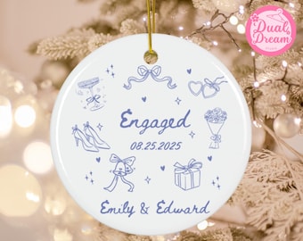 May include: White ceramic ornament with a gold string, featuring blue line art of engagement-themed icons. The word "Engaged" is written in blue script, along with the date 08.25.2025 and the names "Emily & Edward".