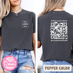 May include: Pepper-colored t-shirt with a square logo area that says "Your Logo Here" on the front. The back of the shirt features a QR code with the text "Follow Us for More!" and a business handle.