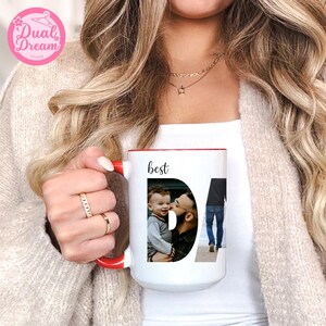 May include: White ceramic mug with a red interior and handle. The mug features the word "best" above a photo collage spelling "DAD". The collage includes a photo of a father and child. The mug is held by a person.