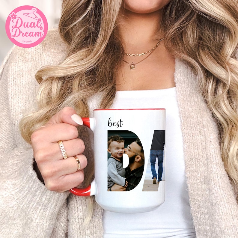 May include: White ceramic mug with a red interior and handle. The mug features the word "best" above a photo collage spelling "DAD". The collage includes a photo of a father and child. The mug is held by a person.