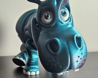 Könnte beinhalten: Eine teal-farbene, cartoonartige Nilpferdfigur mit großen, ausdrucksstarken Augen und einem freundlichen Gesichtsausdruck. Das Nilpferd hat weiße Zähne und Füße, und sein Körper hat ein strukturiertes Aussehen. Die Figur ist ein skurriles Dekorationsstück.
