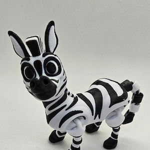May include: A black and white zebra figurine with articulated legs and a tail. The zebra has a friendly expression and is made of plastic.