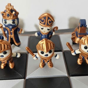 May include: A set of 3D printed chess pieces in gold and blue. The pieces are designed to look like cartoon characters with a whimsical style. The pieces are arranged on a chessboard.