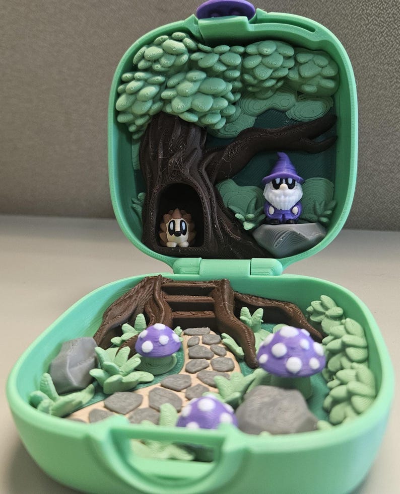 Puede incluir: Una escena de bosque en miniatura dentro de un estuche verde. La escena incluye un &aacute;rbol, setas, un camino y dos peque&ntilde;as figuras: un erizo y un mago. Las setas son moradas con puntos blancos. El estuche est&aacute; abierto, revelando el interior detallado.