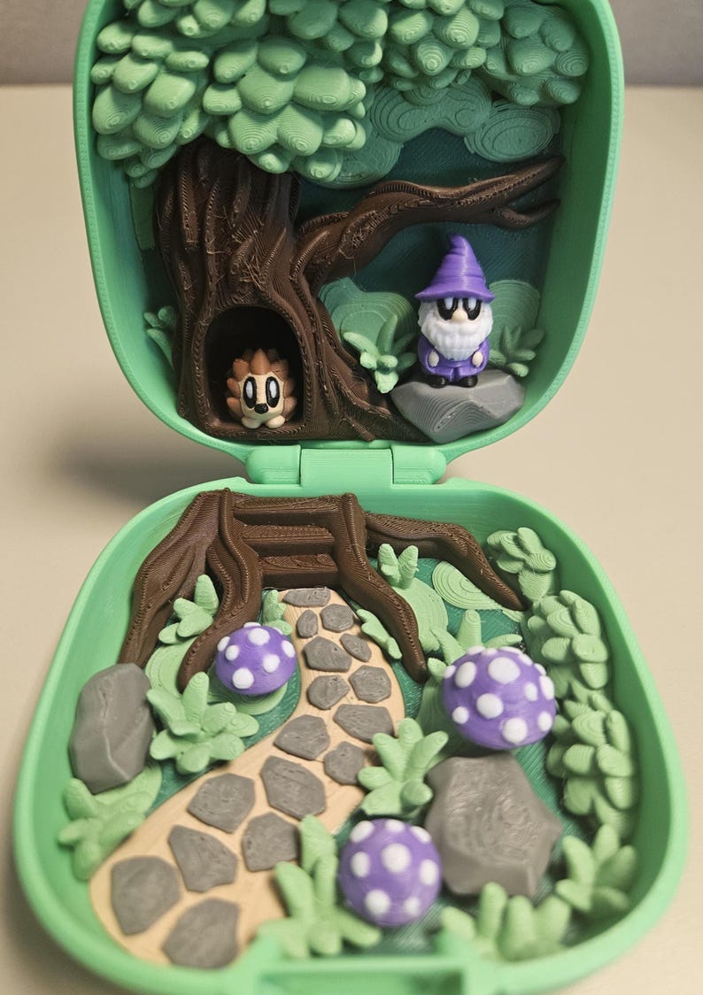 Puede incluir: Una escena de bosque en miniatura dentro de una concha verde. La escena incluye un &aacute;rbol, un gnomo, un erizo, setas y un camino de piedra. El gnomo lleva un sombrero morado y las setas tienen manchas blancas. La concha est&aacute; abierta, revelando el interior detallado.