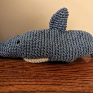 May include: A crocheted blue shark plush toy with a white belly and black eyes.