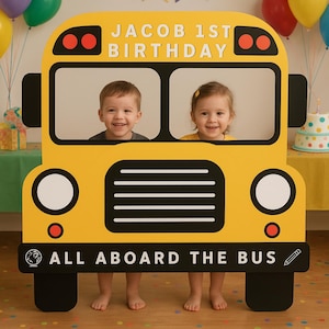 May include: A yellow school bus photo prop with the text "JACOB 1ST BIRTHDAY" at the top and "ALL ABOARD THE BUS" at the bottom. Two children are visible through the bus windows, smiling. The prop has black wheels and details.