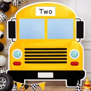 May include: A large yellow school bus cutout with the word "Two" on top. The bus has black accents, blue windows, and red and blue details. Balloons and party decorations are in the background.