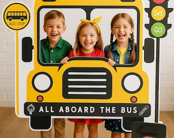 Puede incluir: Tres niños posan para una foto frente a un recorte de cartón de un autobús escolar amarillo. El recorte tiene las palabras "School Bus" y "All Aboard The Bus" impresas en él. Hay un recorte de semáforo a la derecha del recorte del autobús. El semáforo tiene las palabras "Let's", "Set" y "Go" impresas en él. Hay lápices de colores y un portapapeles con una hoja de papel en blanco sobre una mesa de madera frente a los niños.