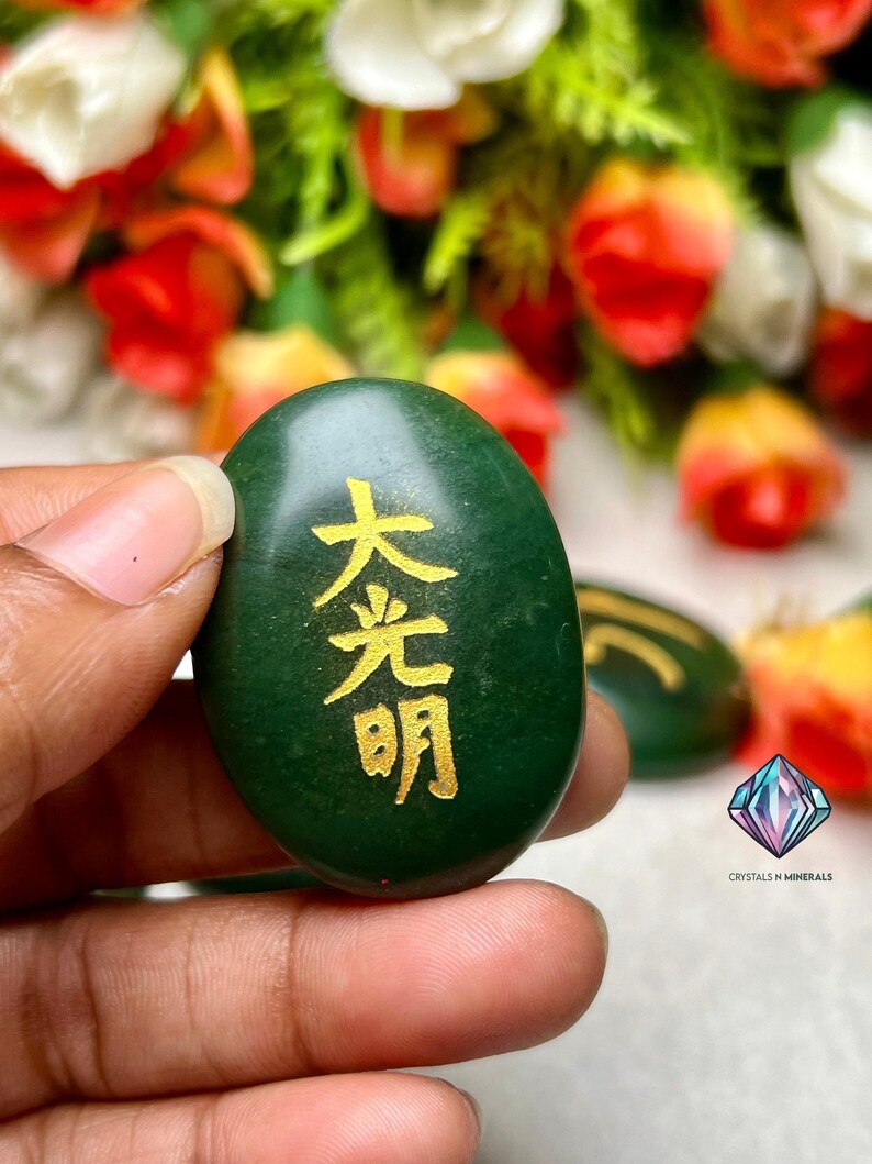 May include: A green oval-shaped stone with gold Chinese characters that read "大光明" (Da Guang Ming) which translates to "Great Light" or "Great Illumination".