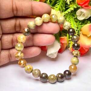 May include: A bracelet made of round, multi-colored, green, brown, and yellow stones.