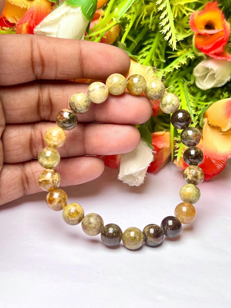 May include: A bracelet made of round, multi-colored, green, brown, and yellow stones.