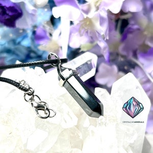 May include: A black hematite point pendant on a black cord necklace. The pendant is sitting on a bed of white quartz crystals. The pendant is a popular choice for those seeking grounding and protection.