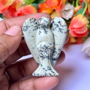 May include: A white and black speckled stone angel figurine. The angel has wings and a long flowing robe. The figurine is carved from a natural stone.
