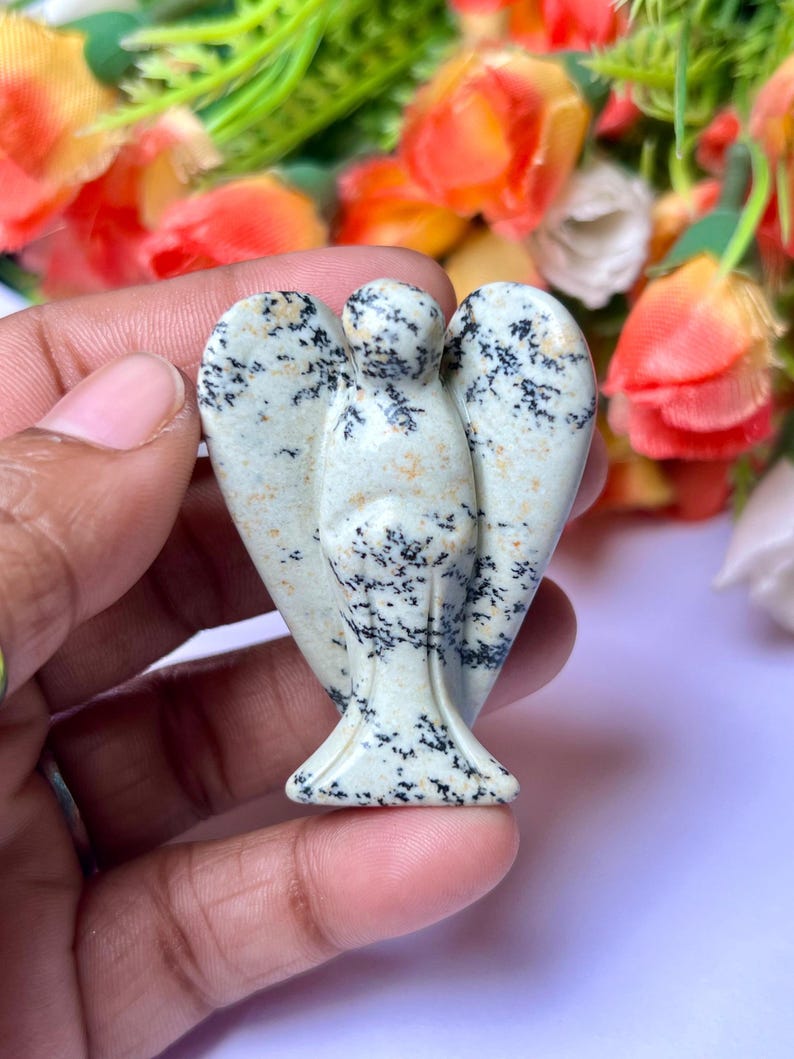 May include: A white and black speckled stone angel figurine. The angel has wings and a long flowing robe. The figurine is carved from a natural stone.