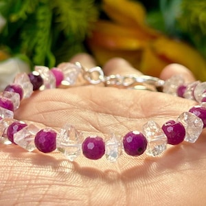 May include: A bracelet made with clear and pink faceted gemstone beads. The bracelet is on a person's wrist.